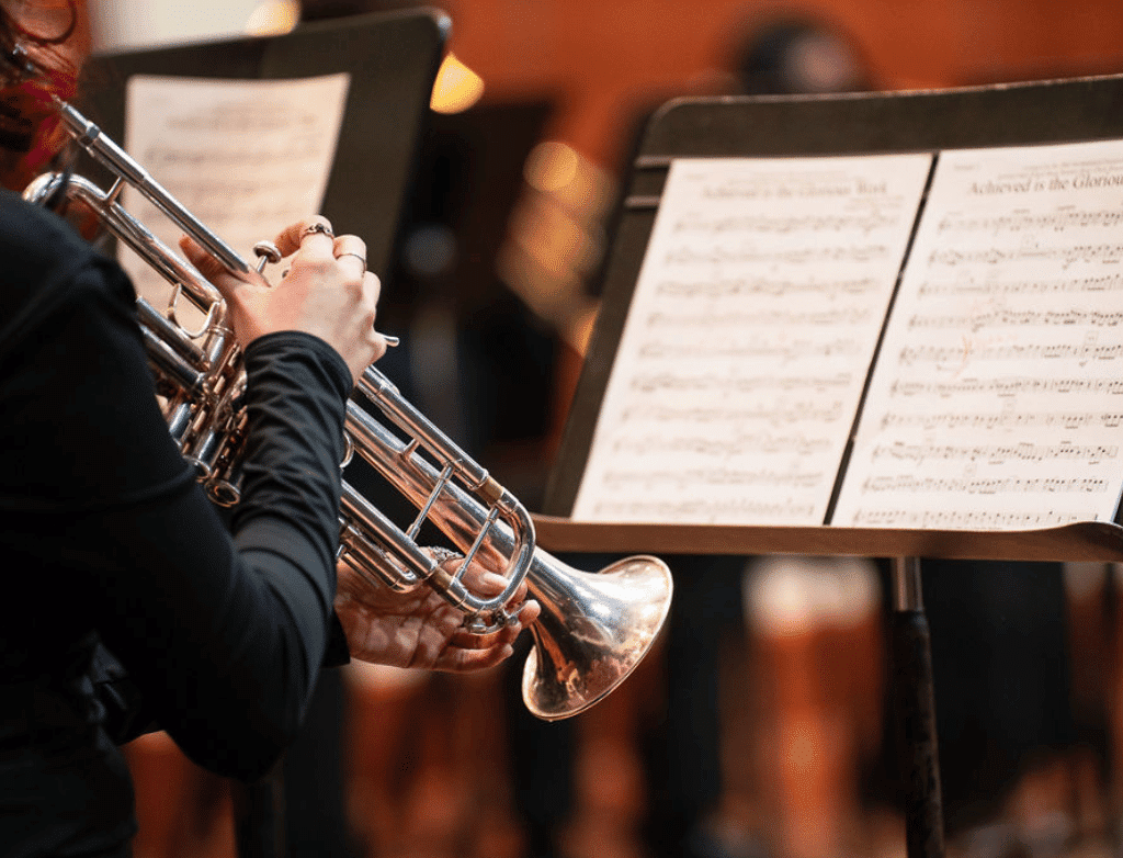 An over-the-shoulder shot of a student playing trumpet. In front of them is a music stand with sheet music.